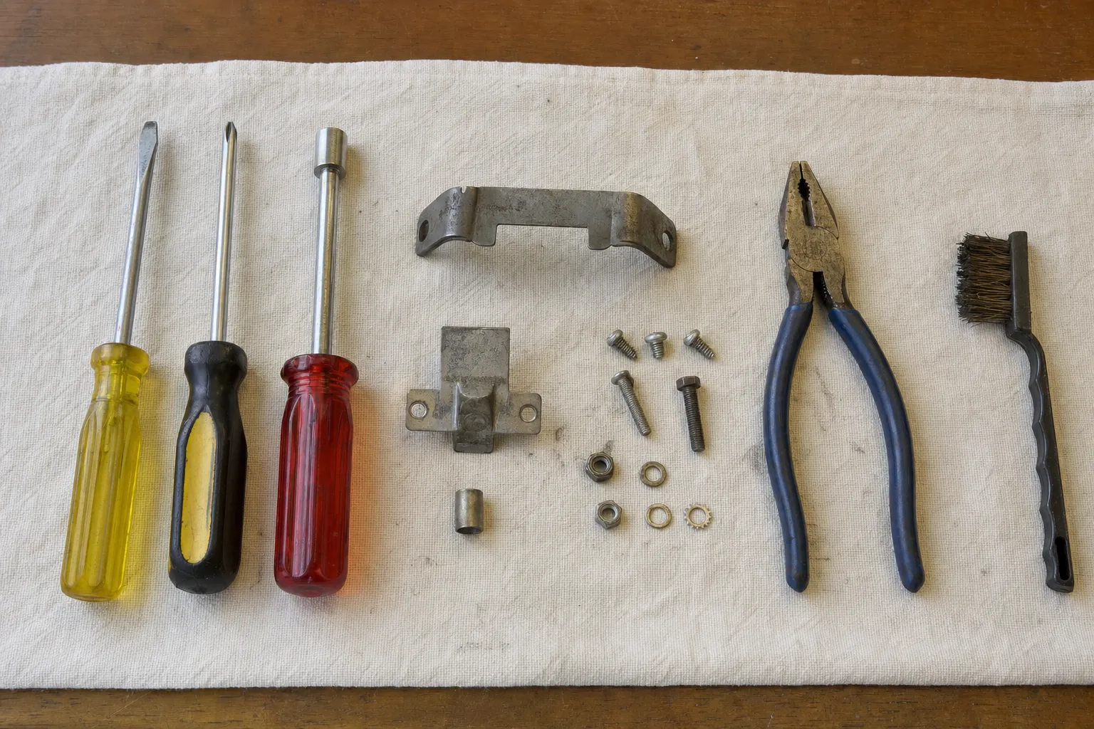 Canvas runner with three drivers in a row, two stamped brackets, a sleeve, screws, nuts and washers, blue pliers and a brass-bristle brush
